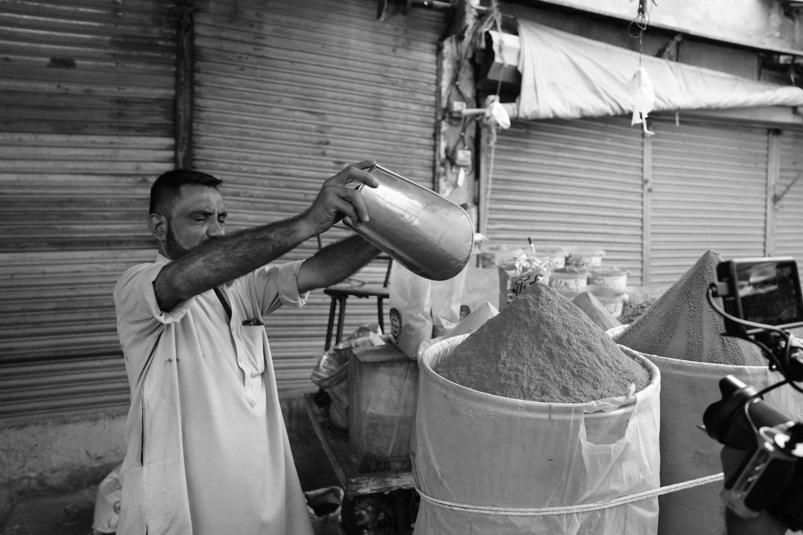 Vendedor de mercado vierte un producto en un saco mientras es fotografiado